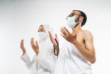 Asian couple wearing ihram clothes and mask with two palms up in prayer on isolated background