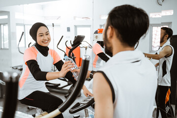 muslim couple exercising together at the gym having a bottle of water while taking a break