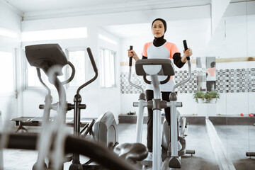 muslim women at the gym doing cardio exercises on static elliptical cycle machine