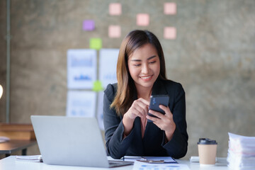 Beautiful Asian businesswoman using smartphone to view social media applications, respond to customer chats, make transactions through an application in the office.