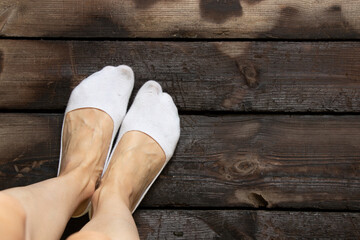 Women's legs and short white socks on the legs on a wooden floor, short socks