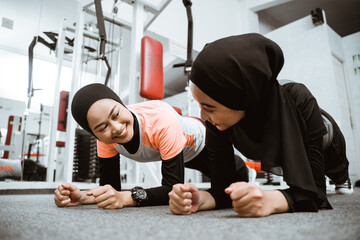 asian muslim woman doing plank push up with partner at the gym
