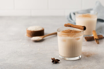Homemade Horchata rice drink in a glass with ice and cinnamon stick on a gray concrete background. Copy space.