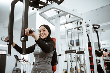 Fototapeta na wymiar muslim asian woman using chest press machine during fitness at the gym