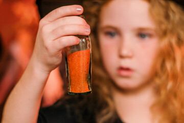 Portrait of a cute red-haired girl in a black witch costume and hat holding a bottle of potion in Halloween decorations.Halloween concept.Selective focus.