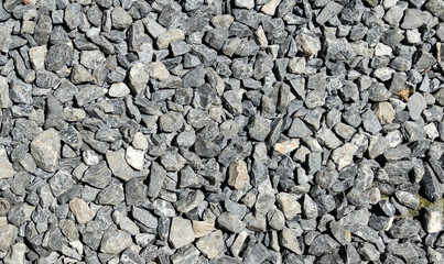 Grey pebbles on the floor against sunlight at noon. Gravel walkway background. The texture of gray gravel on the floor. A random pattern of pebbles.