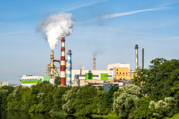 Fototapeta na wymiar pipes of woodworking enterprise plant sawmill with beautiful reflection in blue water of river. Air pollution concept. Industrial landscape environmental pollution waste of thermal power plant
