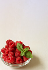 Fresh raspberries in the clear glass bowl on the white background with copyspace
