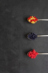 Three spoons with berries (raspberries, blueberries, strawberries) on the black background. Closeup. Flatlay. Copyspace