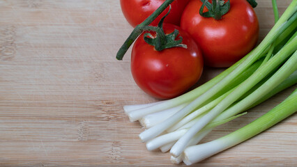 tomatoes on a branch and green onions, vegetables and greens on a wooden background