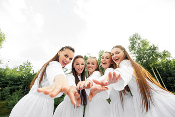 Stylish Ukrainian women in white dresses pose in the yard, stretching out their hands to the camera. Wide viewing angle.