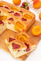 Sponge cake with apricot and strawberry on wooden board. Slice of homemade fruit pie on table.