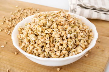 Green buckwheat sprouts in white bowl on wooden board. Natural source of zinc, magnesium and iron. Raw seeds for healthy vegan meal.