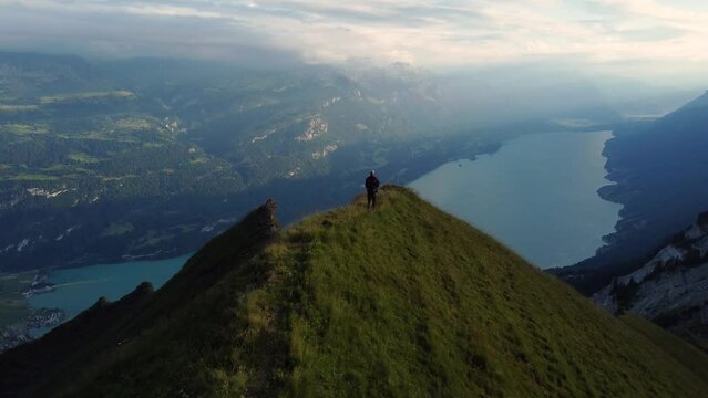 Young mountaineer hiking toward a dramatic mountain cliff in the landscape of Switzerland, with a view of Lake Brienz during sunset hours, after a successful and adventures hike in the Alps