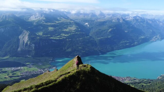 Aerial drone shot of a man standing on a cliff on a clear blue day with a view of the scenery of Lake Brienz, close to Brienzer Rothorn and the stunning European Alps of Switzerland