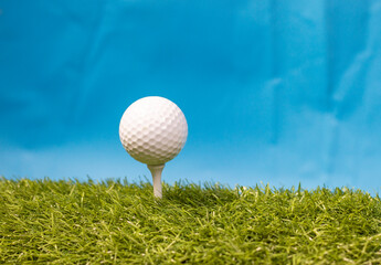 Golf ball on tee ready to tee off on green grass with blue sky background