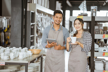 Boy and girl wearing aprons smiling while holding a pad and holding a cup in houseware store