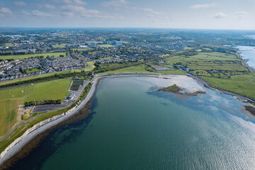 Fototapeta premium Aerial view on Ballyloughane Strand in Galway city, Ireland. High tide. Blue cloudy sky and ocean water. Popular area with amazing view and footpaths for walk close to Renmore residential area