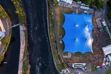 Fotobehang Concert of beer festival area with big blue tent and service areas by a river. Big crowd enjoy all amenities. Aerial top down view. Music event or circus in town. Entertainment industry and business. © mark_gusev
