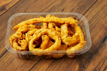 Onion rings serving in a plastic tray on wooden table surface background. Simple food with high calorie and fat count. Beer snack.