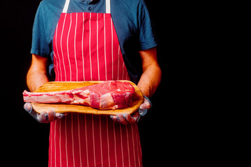 Butcher holding wooden board with raw tomahawk steak on the bone and black background. Prime cut of...