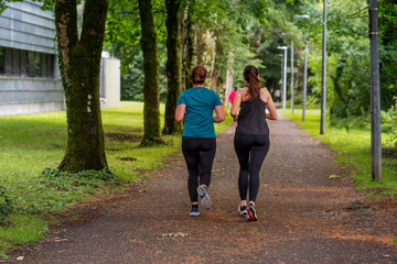 Fototapeta premium Two woman running on a footpath in park. Back to camera. Active and healthy lifestyle concept. Jogging to stay positive and increase endurance. Selective focus.