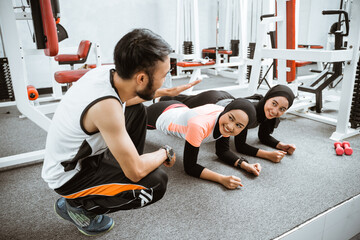 two muslim woman doing plank at the gym with trainer teaching them