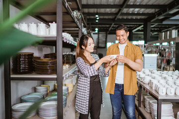 Fototapeta na wymiar Young asian woman and young man holding ceramic cups while choosing cups in houseware store
