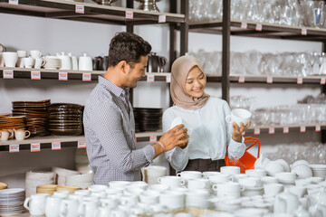 Young muslim woman holding cup while selecting crockery with her male friends in houseware store