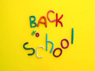 letters made of multi-colored plasticine back to school in wry funny style on yellow background
