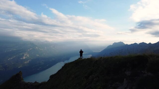 Hiker standing on top of a mountain peak in the Alps of Switzerland, with the sunset view overlooking Lake Brienz with a feeling of freedom, success, achievement and full of adventure
