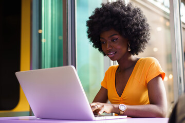 Happy beautiful young black woman using laptop in cafe - Powered by Adobe