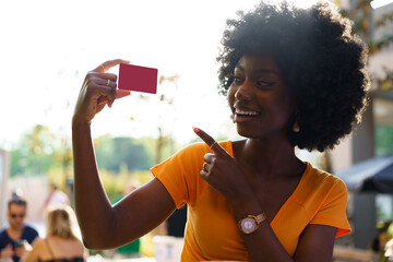 Portrait of young american woman with afro hairstyle holding red plastic credit card