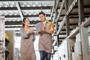 Young asian couple wearing apron chatting while using tablet in houseware store