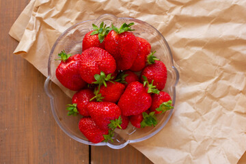 Many red strawberries on glass plate and wooden table top view