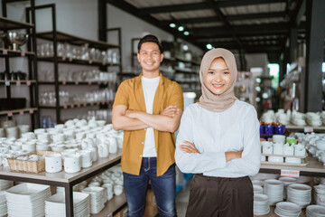 beautiful asian muslim woman smiling while standing with hands crossed in glassware store