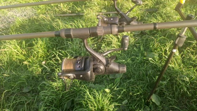 Unwinding fishing line or cord from a reel spool for rod pod against the background of green grass. Fish biting on a sunny summer day. Catching carp and pike on a spinning reel with a baitrunner