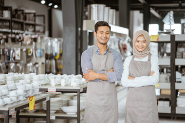 Shop assistant boy and girl in veil standing with arms crossed in houseware store
