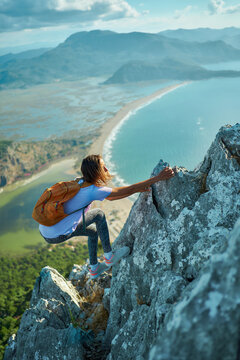 Vertical image active woman climbing up on cliff over beautiful beach with sea and mountain range. Outdoors activity by traveling in Turkey at summer