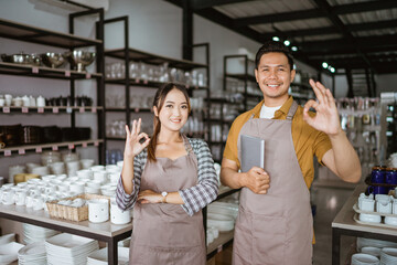 Two shop owners in apron holding digital tablet standing with okay hand gesture in houseware store