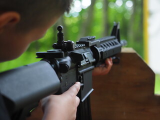 The barrel of a gun is held by a child in his hands, aims at the target