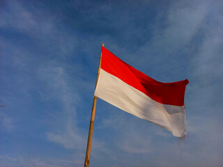 A waving Indonesia national flag in a bamboo-made flagpole with a blue sky as the background.