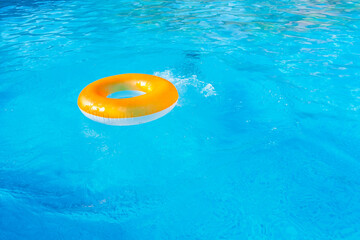 A white-orange inflatable ring on the blue water in the pool and a child diving under the water