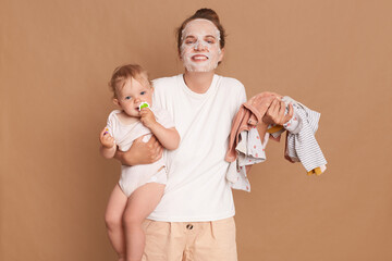 Happy positive woman wearing white t shirt doing cosmetic procedures while playing with kid and...