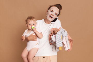 Amazed woman wearing white t shirt doing cosmetic procedures, holding baby daughter in hands and...