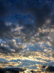bright summer blue sky with white fluffy clouds of various shapes and sizes, cirrus, heap clouds, golden from sunlight.