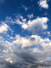 bright summer blue sky with white fluffy clouds of various shapes and sizes, cirrus, heap clouds, golden from sunlight.
