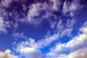 bright summer blue sky with white fluffy clouds of various shapes and sizes, cirrus, heap clouds, golden from sunlight.