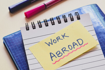 Sticky note with the text Work Abroad on office desk.