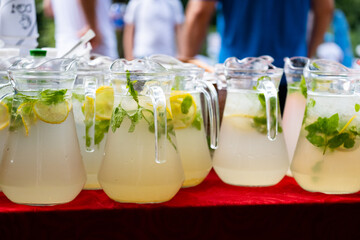 Many juges with lemonade on table at meeting or party outdoors. Summer refreshing drink. Cold detox...